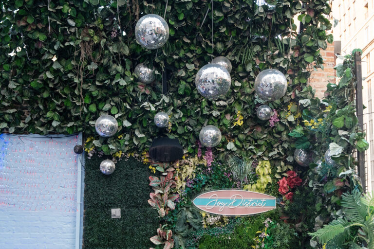 Greenery wall with disco balls and the Joy District sign at the AWE Symposium reception at Joy District, Chicago