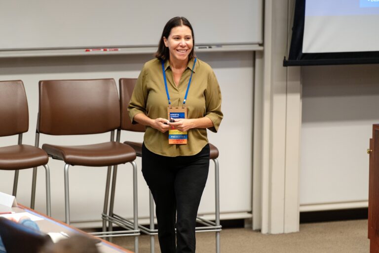 Presenter smiling at the front of a session room at Gleacher Center