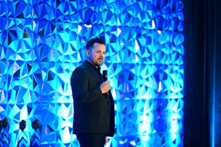 Speaker on stage in front of a lit backdrop at an awards event – Creative Soul Studios