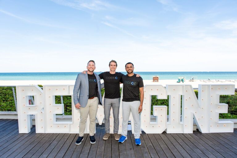 Team posing at the oceanfront Reimagine sign at NeoSummit