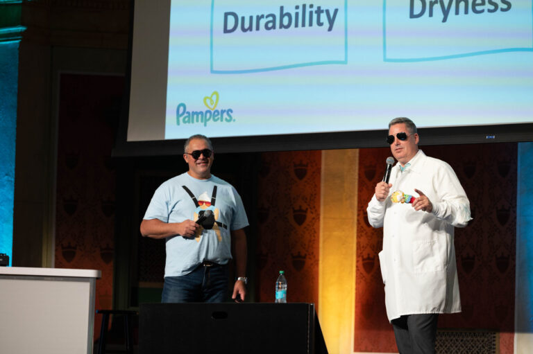 Two presenters on stage with a Pampers slide at the P&G Baby Care event, Music Hall Cincinnati