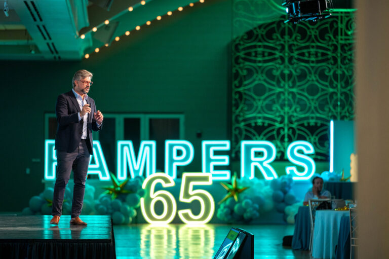 Speaker beside the Pampers 65 neon sign at the P&G Baby Care event, Music Hall Cincinnati